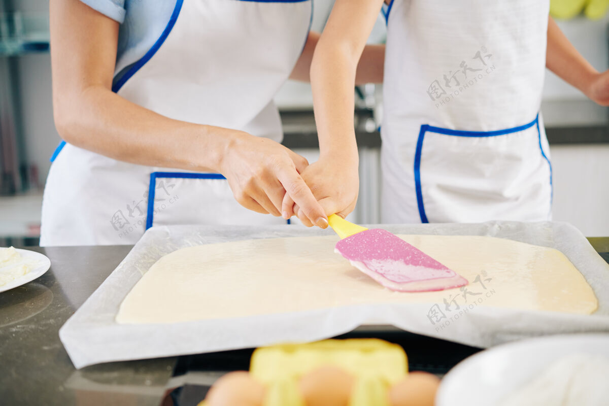 甜点特写图片的母亲帮助女儿分发液体面团在烤板用硅胶抹刀蛋糕烘焙家庭主妇