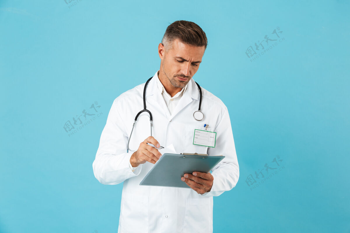 专家高加索医生手持听诊器手持健康卡 孤零零地站在蓝色墙壁上的画像医生外套成熟