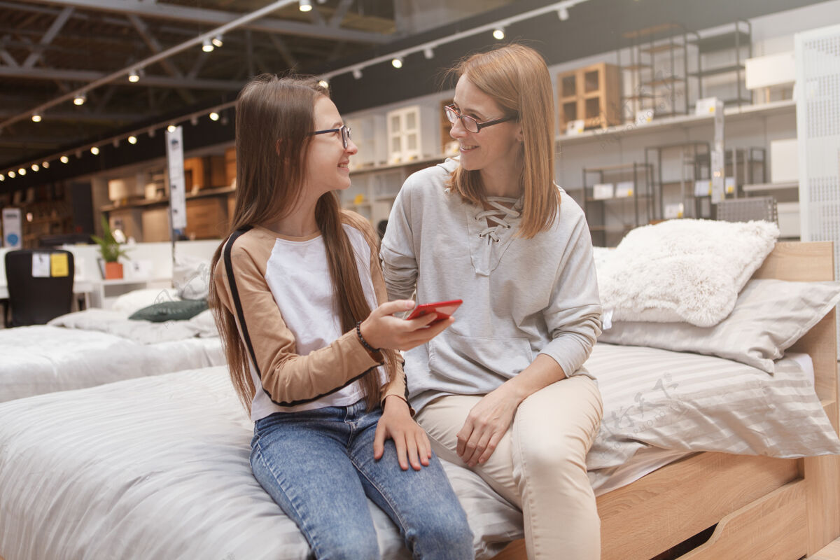 商店十几岁的女孩和她妈妈一起用智能手机聊天消费主义父母在线