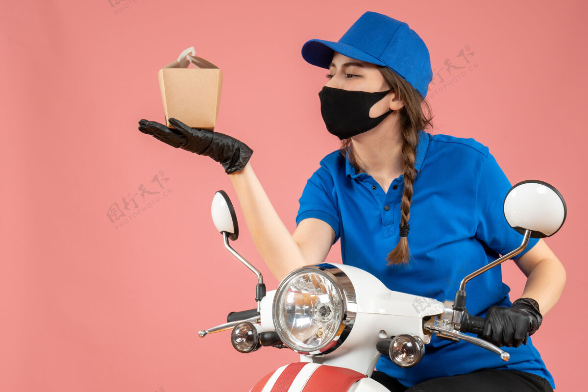 面具女快递员戴着黑色医用口罩和手套拿着桃色背景的小盒子的正视图持有金属手套