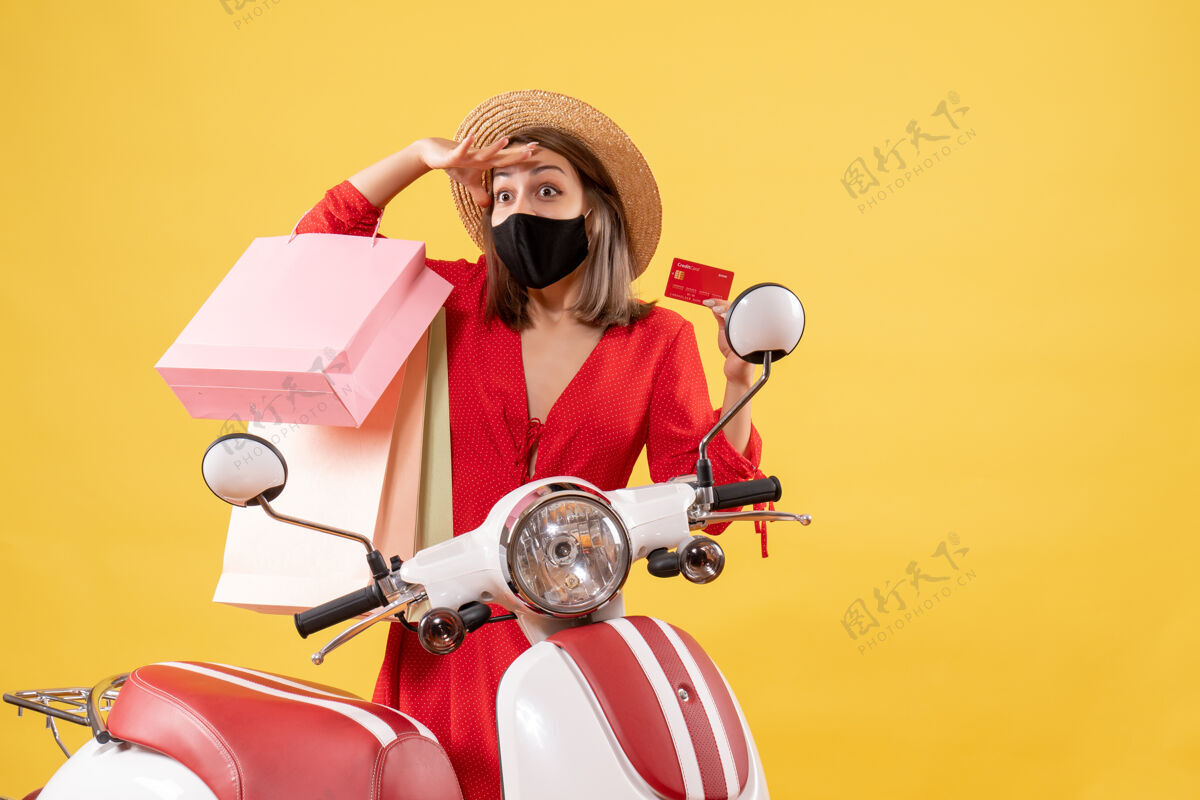 车辆看着戴着黑色面具的年轻女子拿着信用卡和购物袋靠近轻便摩托车黑色摩托车信贷
