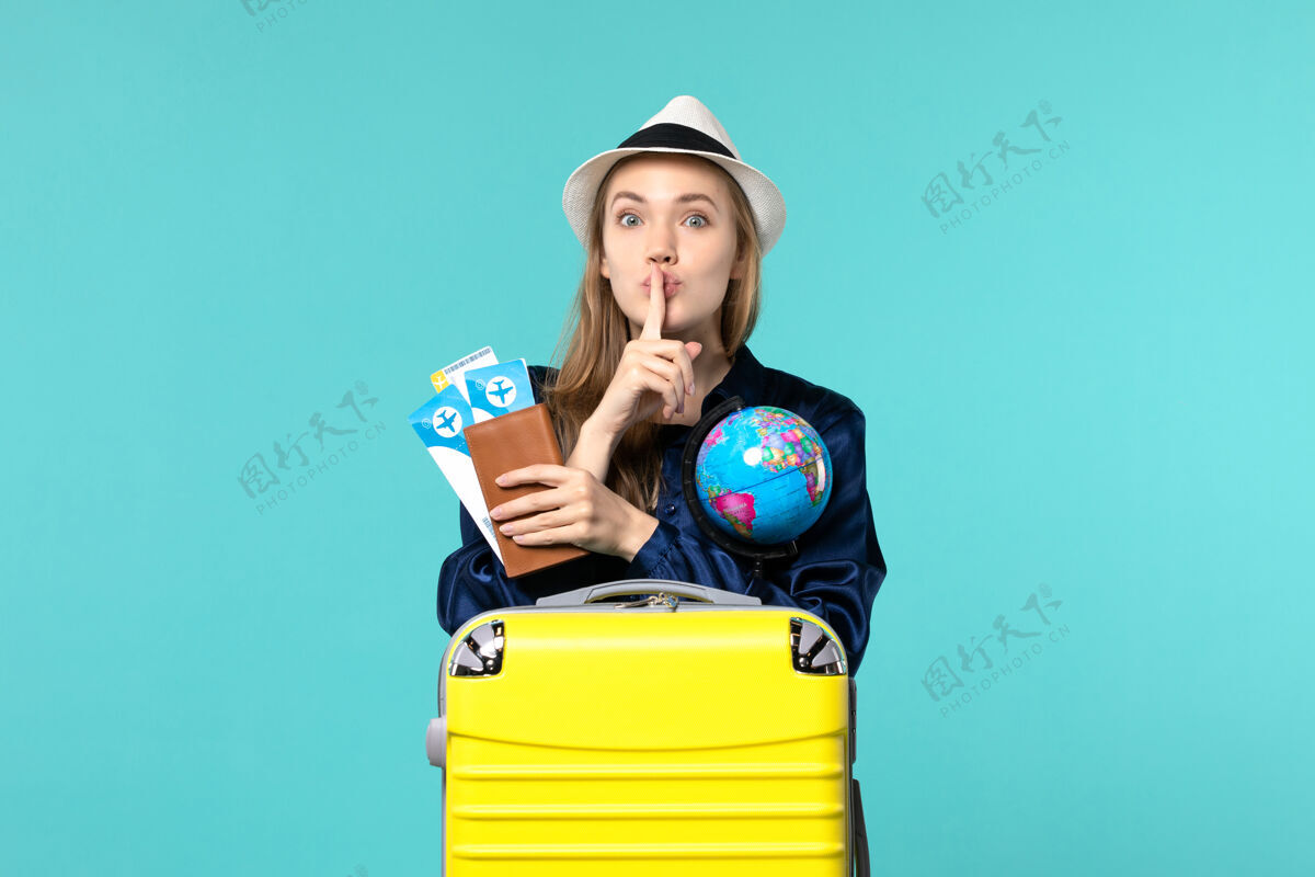 年轻女子正面图年轻女子拿着机票和地球仪在蓝色背景的飞机上海上度假旅行肖像航程举行