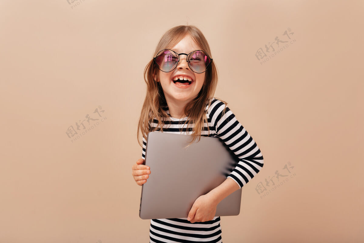 笔记本电脑微笑着兴奋的小女孩戴着眼镜和脱光衬衫笑着拿着笔记本电脑孩子金发微笑