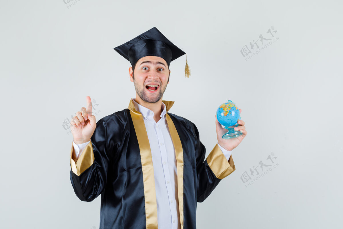 肖像一个穿着研究生制服的年轻人拿着学校的地球仪 指着头 看上去很高兴 正对着前方男人英俊男人