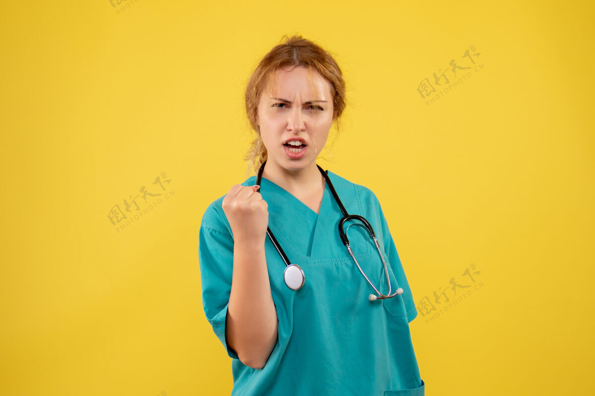 医疗器械黄色墙壁上穿着带听诊器的医疗服的女医生的正视图病毒医疗药品