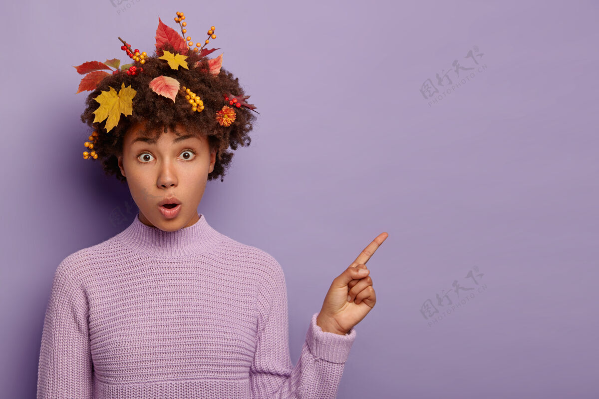 木僵惊讶的黑皮肤女人的肖像点在复制空间 张开嘴 有秋天的叶子和浆果粘在头发上 站在无语和印象深刻 穿着针织紫色毛衣时尚紫罗兰兴奋