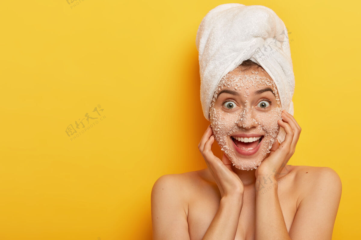 站立快乐可爱的女人 表情愉快 敷天然海盐面膜 拥有健康呵护的肌肤 头戴毛巾 享受卫生治疗人请恢复活力
