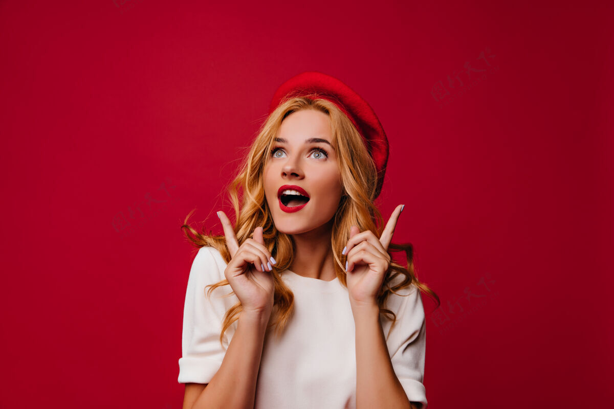 金发温文尔雅的法国女孩在红墙上摆姿势穿着优雅贝雷帽的梦幻女孩表达真诚的情感时尚卷发兴奋