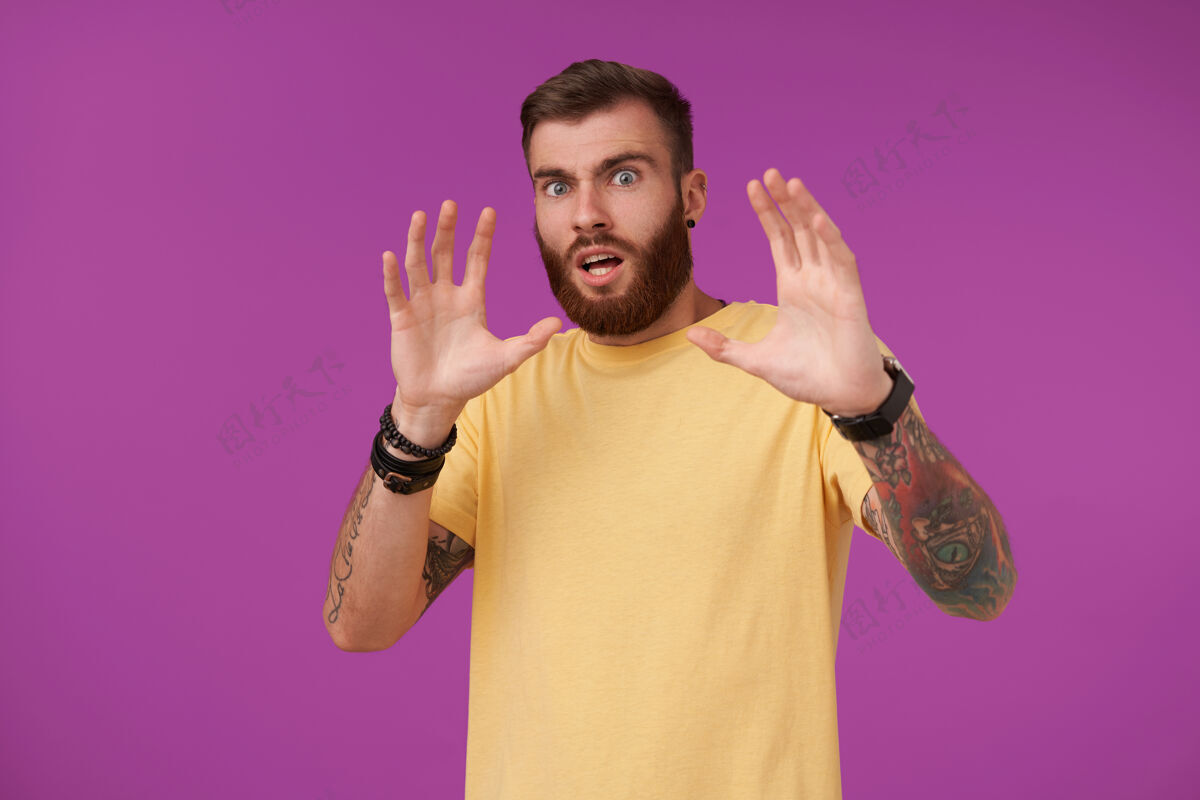 短裤一个留着短发的黑发男人站在紫色的黄色t恤上 眼睛刺青 头发黝黑 脸上没有剃须 看起来很害怕 举手保护自己男性身体站着