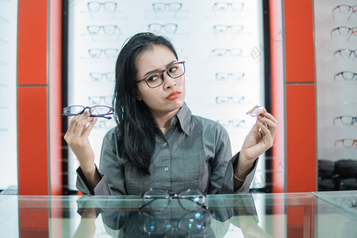 眼镜一个拿着两副眼镜的女人对在眼镜店选购一副新眼镜感到困惑顾客视力选择