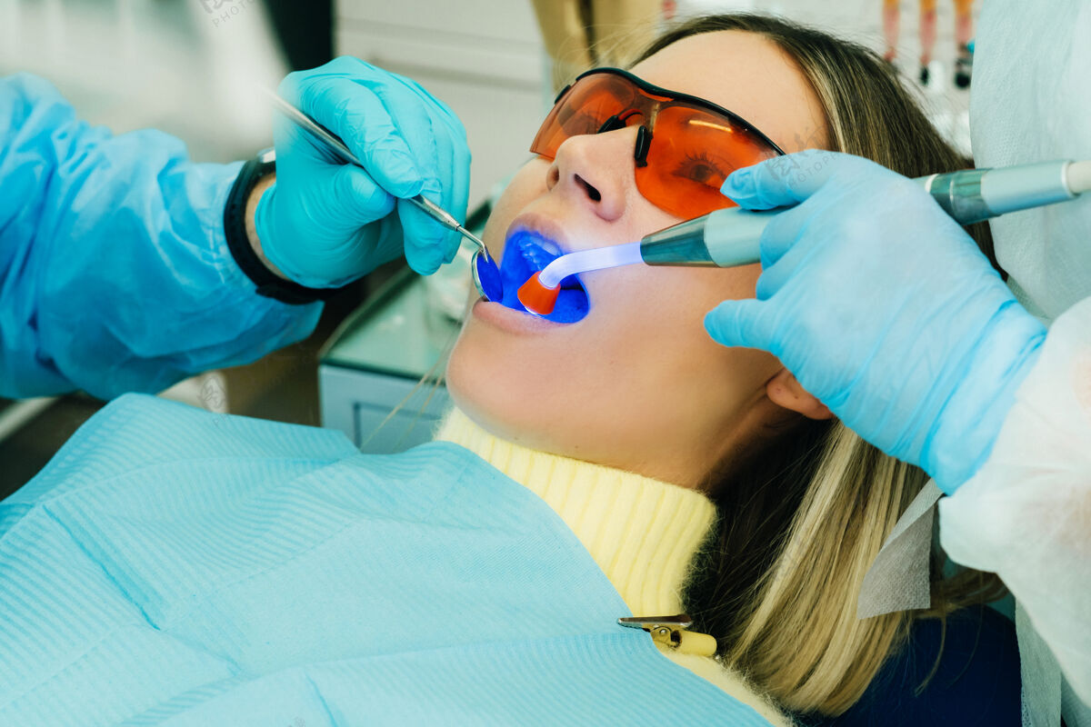 正畸一个戴着眼镜的年轻漂亮女孩在牙医那里用紫外线治疗她的牙齿就诊药品设备