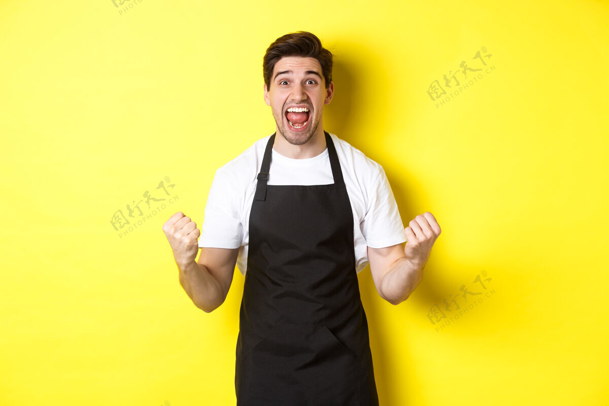 男人兴奋的咖啡店老板穿着黑色围裙庆祝工人生活方式员工