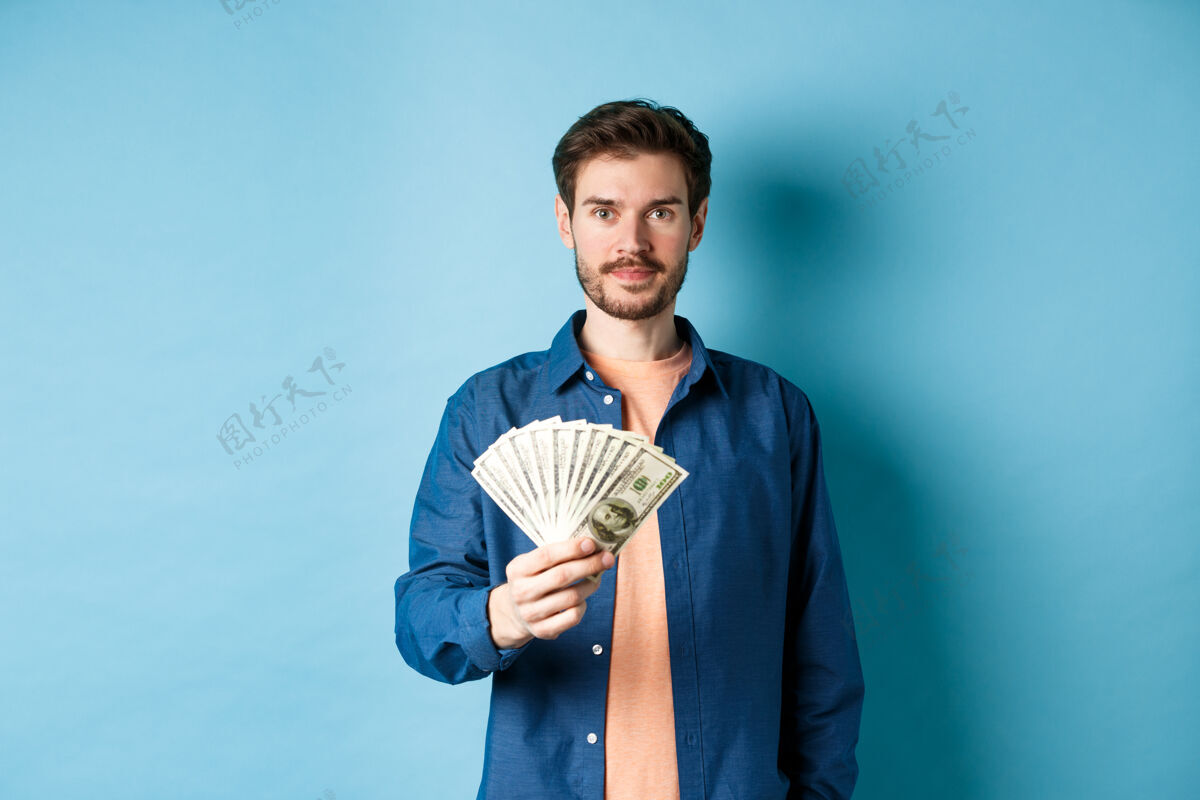成人快乐的现代人拿着钱 微笑着 站在蓝色的背景上现金酷立场