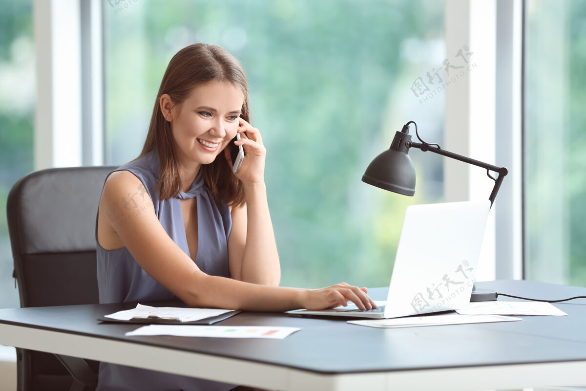 公司办公室里用手机交谈的年轻女商人职业工作桌子