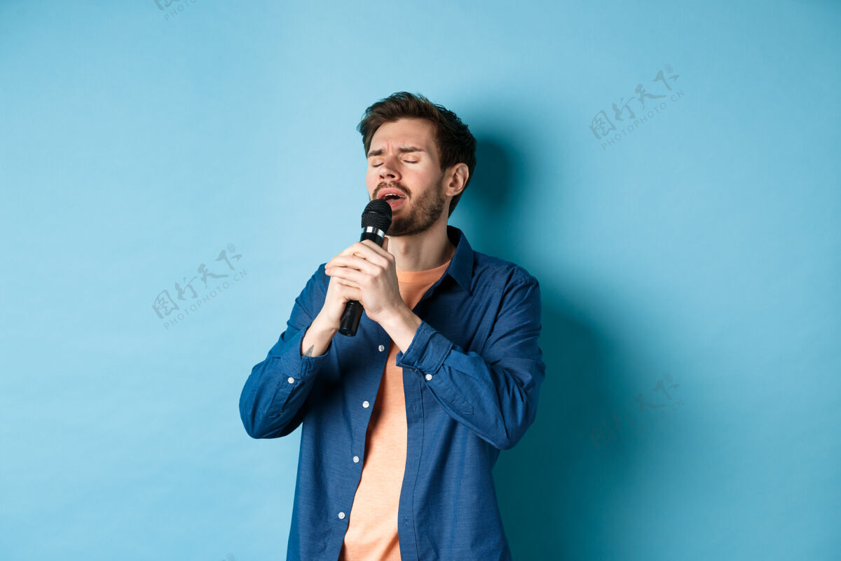 酷浪漫的家伙在麦克风里唱歌 在舞台上表演 站在蓝色的背景上时尚情感卡拉OK