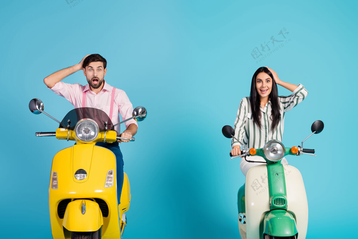 轻便摩托车惊讶的打动了两个人骑自行车的男人女人开摩托车摸头摸手看不可思议的自然景观尖叫哇天哪穿正装衣服隔着蓝色的墙惊人男孩摩托车