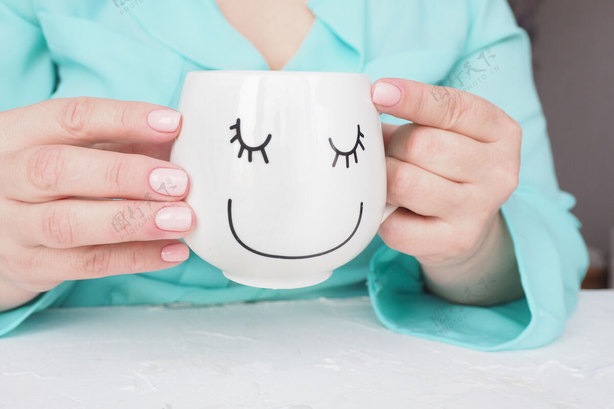 手美丽的美甲和柔软的粉红色指甲油的女性手拿着一杯咖啡或茶 一张有趣的画脸美甲咖啡衬衫