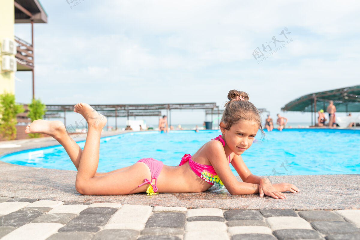 操场穿着粉色泳衣的可爱小女孩躺在游泳池边 在灿烂的阳光下晒太阳泳装可爱跳跃