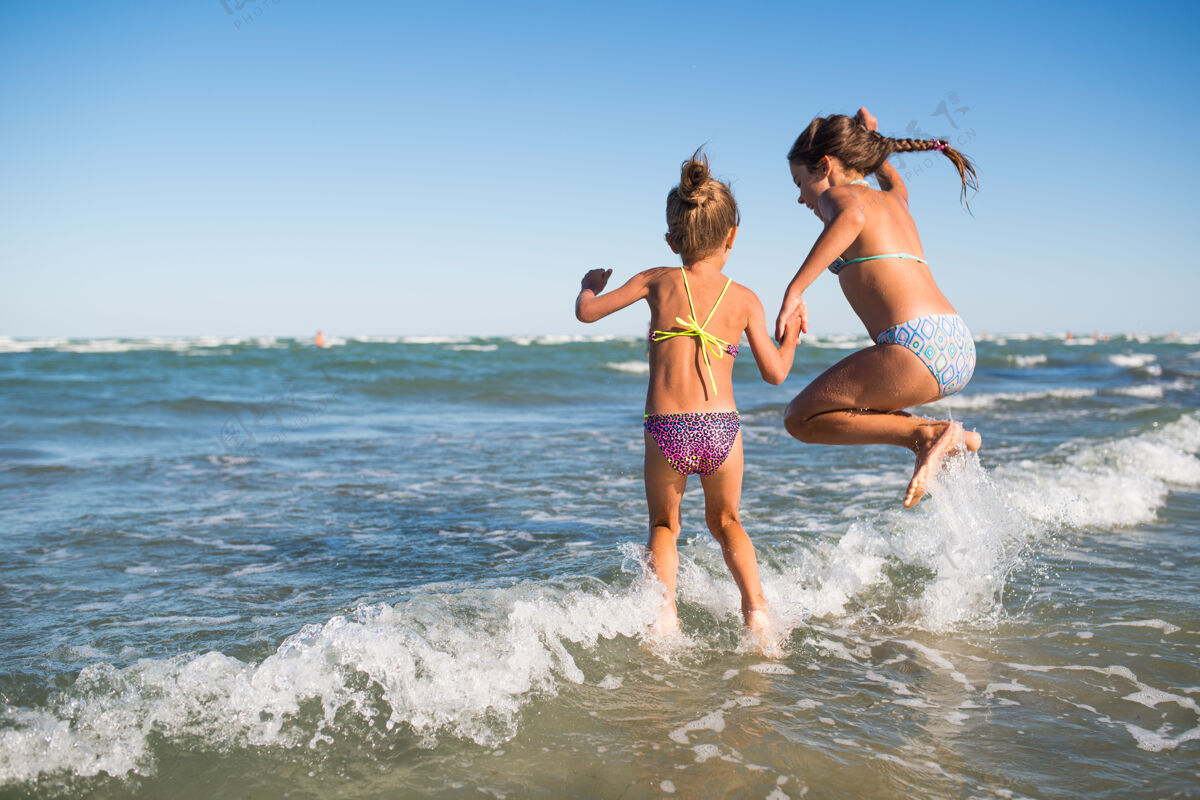 乐趣两个有趣的小女孩在喧闹的海浪中跳跃 在一个阳光明媚的夏日享受期待已久的假期休息海洋泡沫