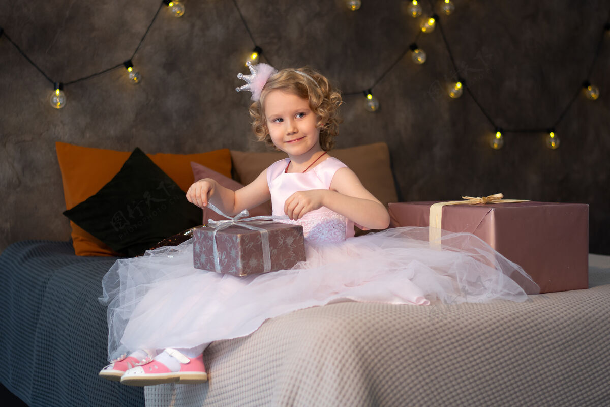 女儿一个穿着粉色裙子戴着皇冠的小女孩在床上放着礼物房间问候装饰