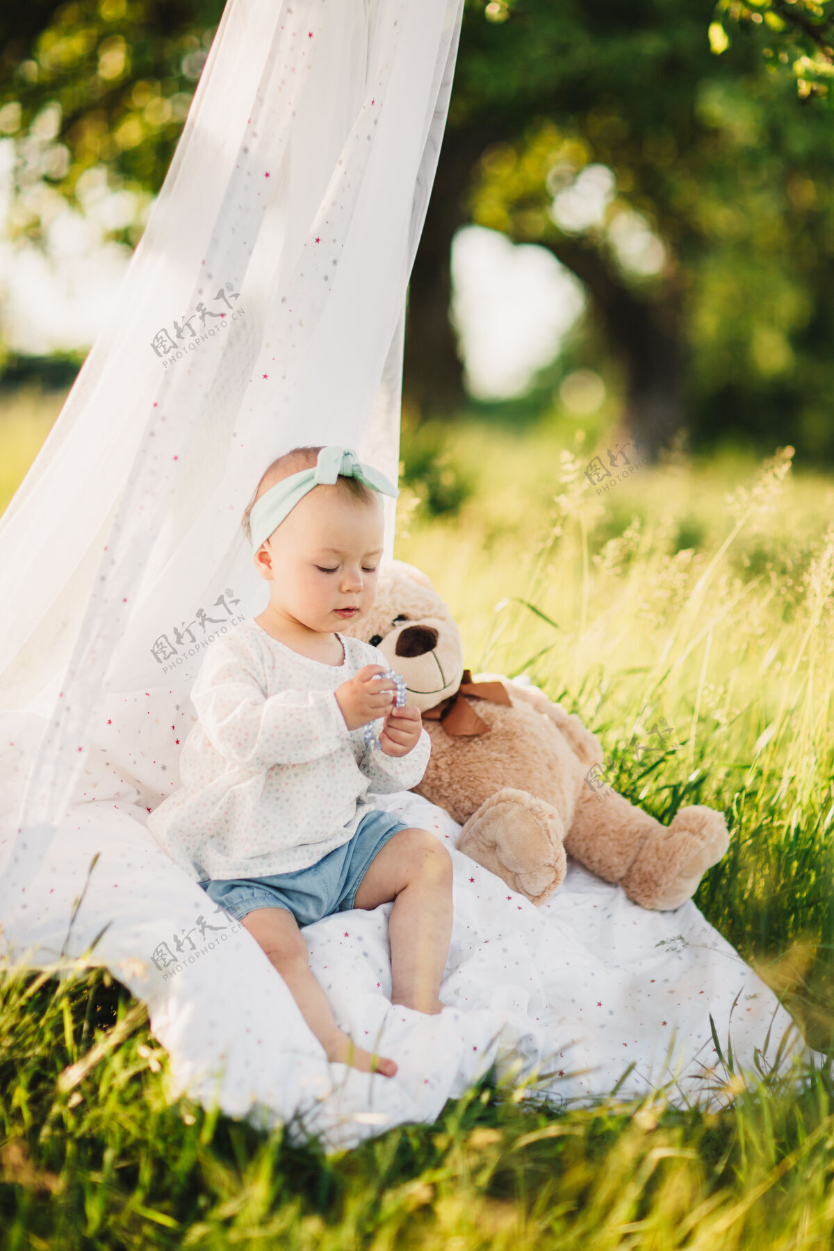 可爱带着泰迪熊的小女孩坐在夏日阳光公园的白色毯子上快乐夏天脸