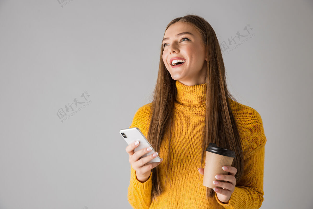 手机一个美丽快乐的年轻女子隔着灰墙用手机喝咖啡的画面黑发休闲饮酒