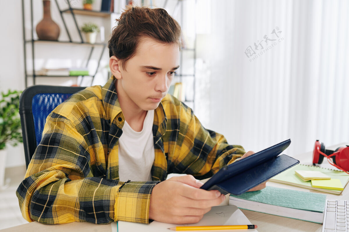 教育由于冠状病毒的流行 严肃的青少年男孩在平板电脑上读学生的书和在家上学书籍笔记本电脑小工具