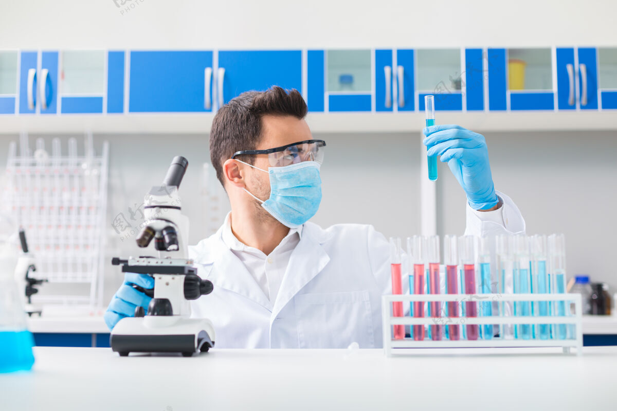室内科学挑战帅气的男实验员戴着安全眼镜 一边抬起瓶子 一边注视着它专家实验室生物化学
