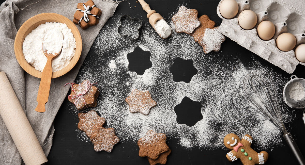 糖烤星型姜饼饼撒上糖粉放在一张黑桌子和配料上 顶视图庆祝霜烘焙