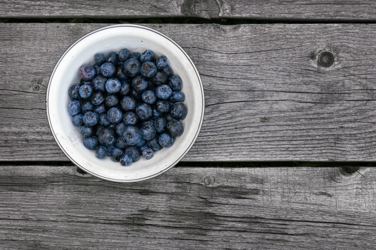 美味新鲜成熟的蓝莓放在一个白色的碗里 放在粗糙的木板上成熟营养堆
