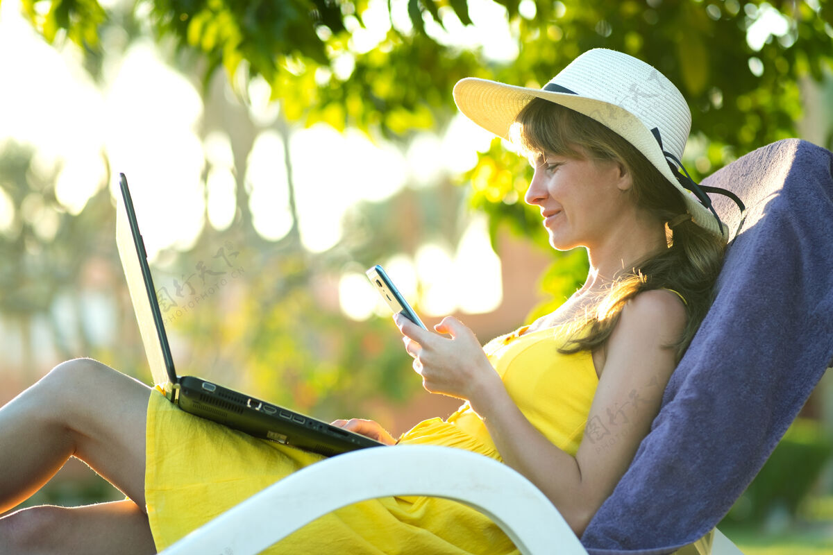 文本穿着黄色夏装的女生在公园的绿色草坪上休息 用笔记本电脑学习 用手机发短信工作公园健康