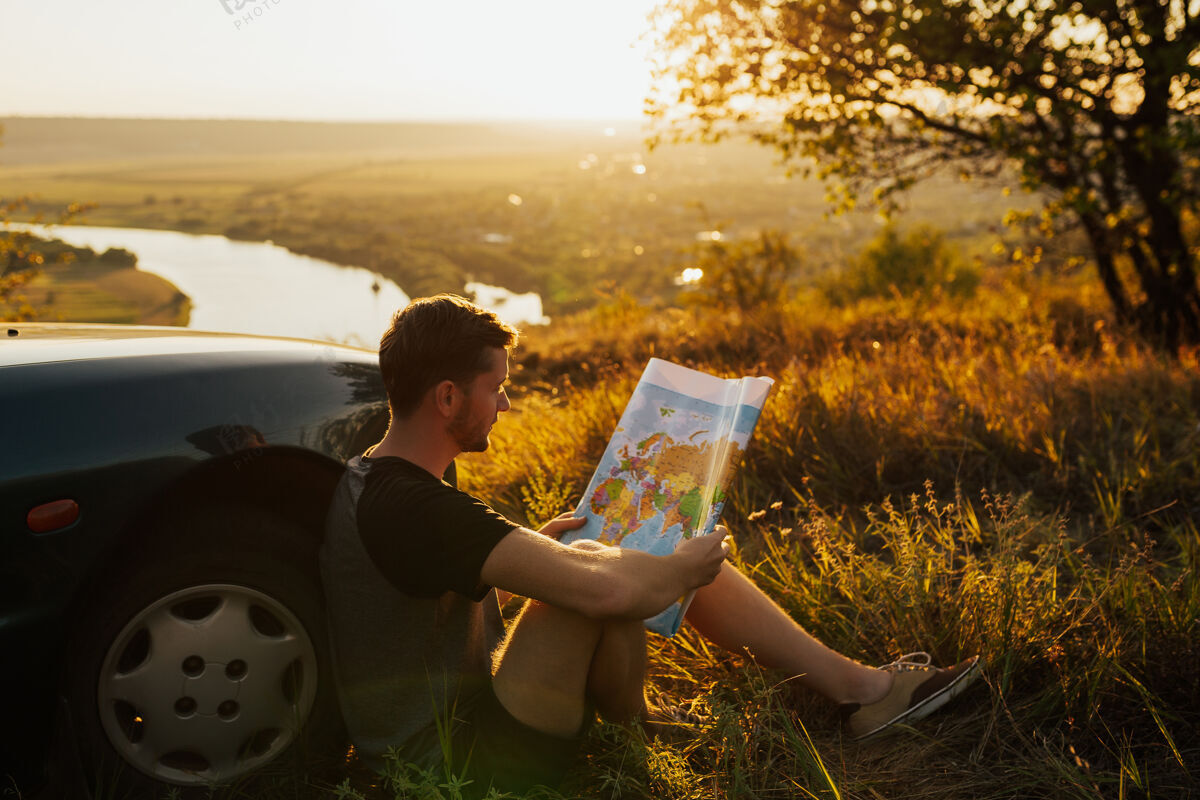 自然日落时分 一个年轻时髦的男人拿着地图在他的车旁边放松风景华丽