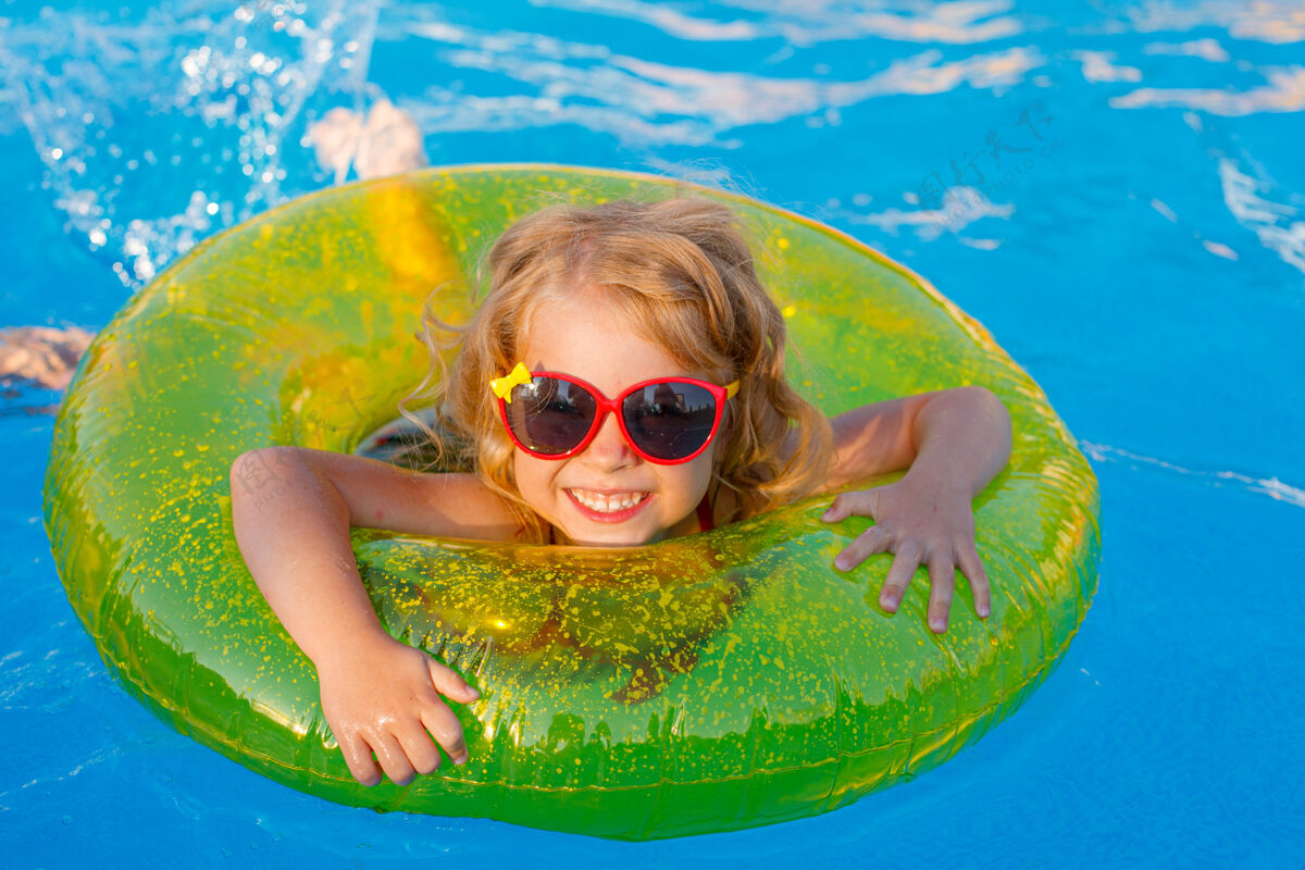 儿童夏天 一个戴着太阳镜和泳衣的小女孩在一个充气圈的游泳池里游泳年轻人可爱欢笑