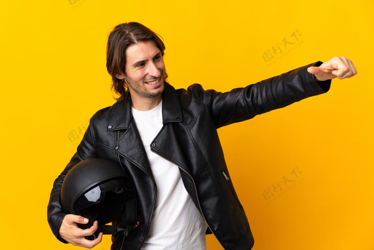 好一个戴着摩托车头盔的男人站在黄色的墙上竖起大拇指男人摩托车手头盔