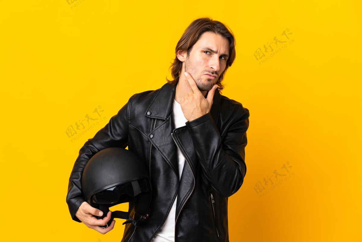 驾驶一个戴着摩托车头盔的男人被隔离在黄色的墙上 他有疑问忽略困惑表情