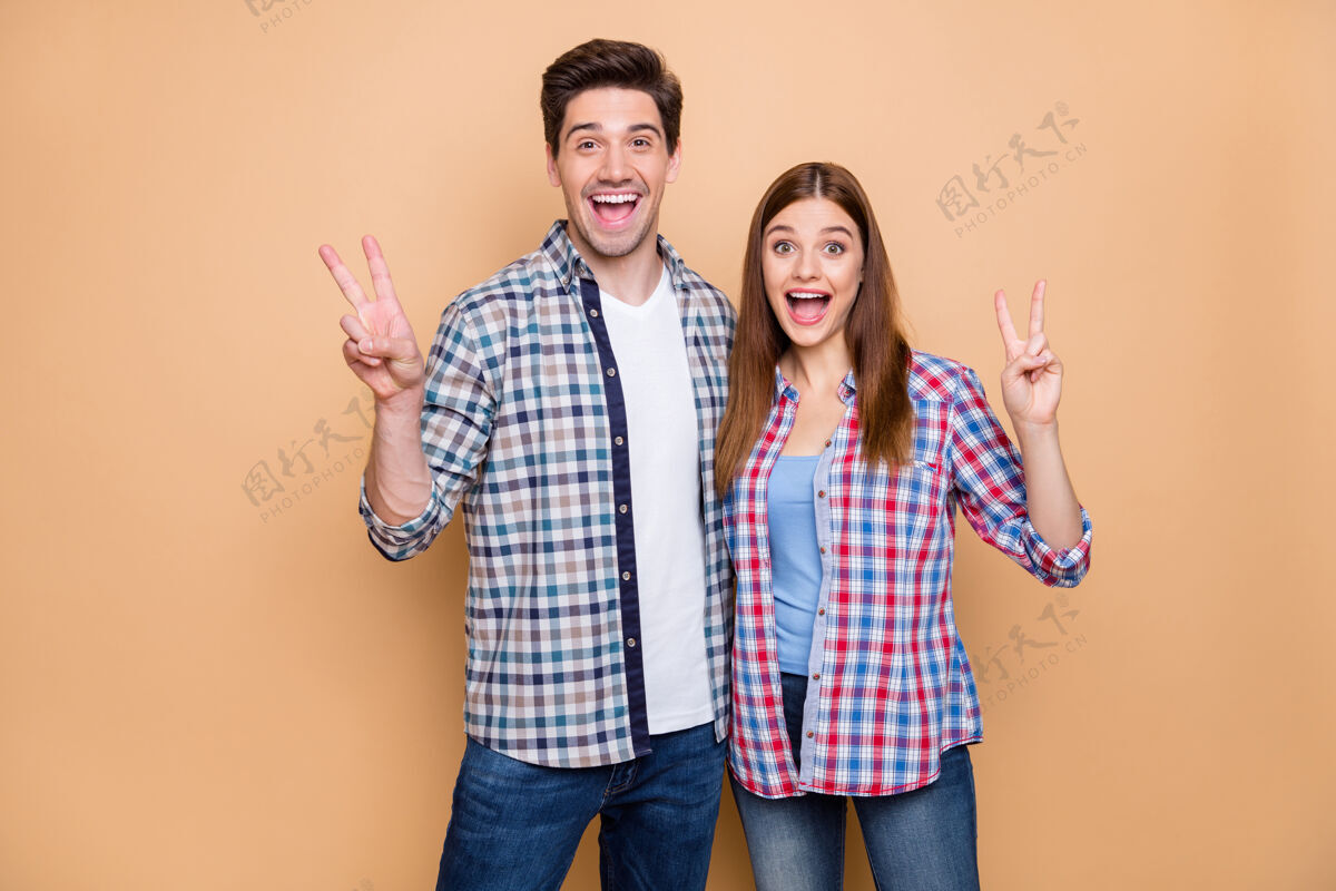 拥抱他\/她漂亮迷人迷人时髦快乐欢快的夫妇的肖像 穿着格子衬衫 显示v形标志拥抱 米色粉彩背景下孤立朋友在一起手势