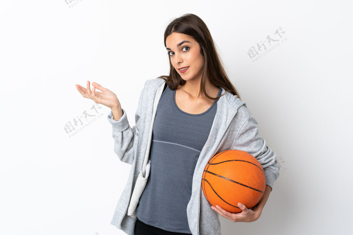 健身打篮球的年轻女子孤零零地站在白色的背景上 向侧面伸出双手 欢迎前来生活方式女性游戏