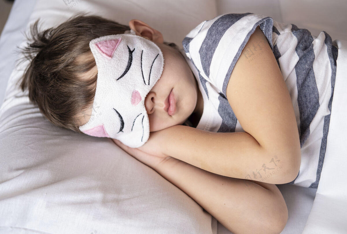 每天高加索学龄前男孩在猫咪眼罩条纹睡衣睡在白色的床上童年睡觉时间孩子