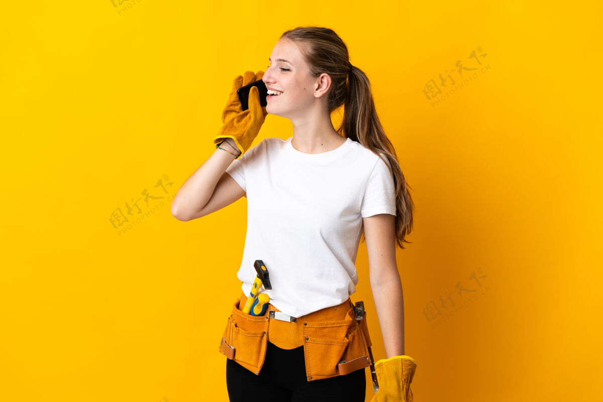 电话被隔离在黄色背景下的年轻电工女人用手机交谈车间工人年轻
