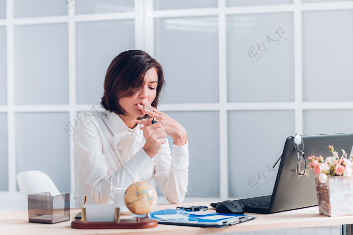 笔记本电脑漂亮的女商人在办公室的办公桌旁抽烟和工作女性工人商业