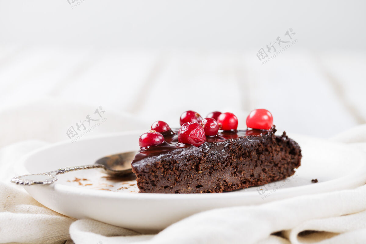 布朗尼一块不含麸质的巧克力糖衣布朗尼蛋糕 用小红莓装饰 放在白色盘子里 放在一张轻薄的木桌上-向上模糊浅色背景健康甜点釉面蔓越莓椰子糖