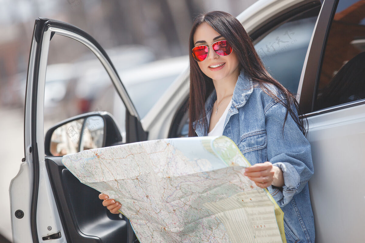 女人年轻游客迷路了镇上的女人举办地图驱动程序得到了迷失方向在外星城市交通开车旅游