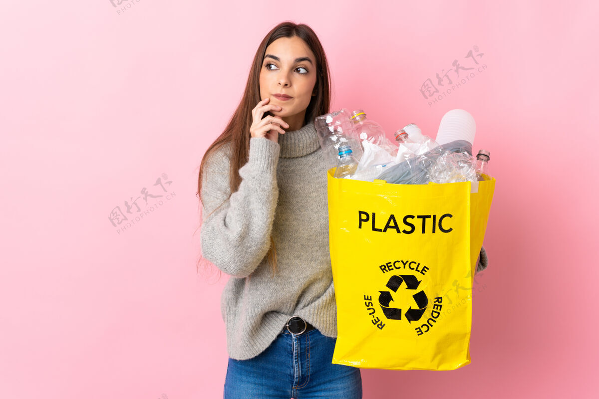奇迹年轻的高加索妇女拿着一个装满塑料瓶的袋子 在粉色背景下 一边抬头一边思考着一个想法黑发解决方案环境