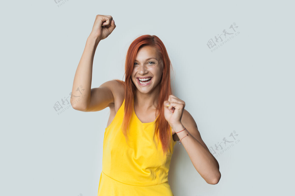 手势一位红发白种女人穿着裙子在白墙上微笑着做着胜利的手势成就脸室内