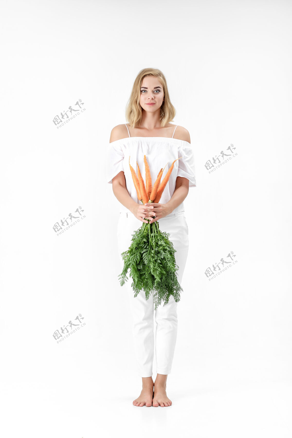 欢呼一个穿着白衬衫的金发美女 手里拿着一根新鲜的胡萝卜 上面有绿叶背景.健康还有节食白色成人素食
