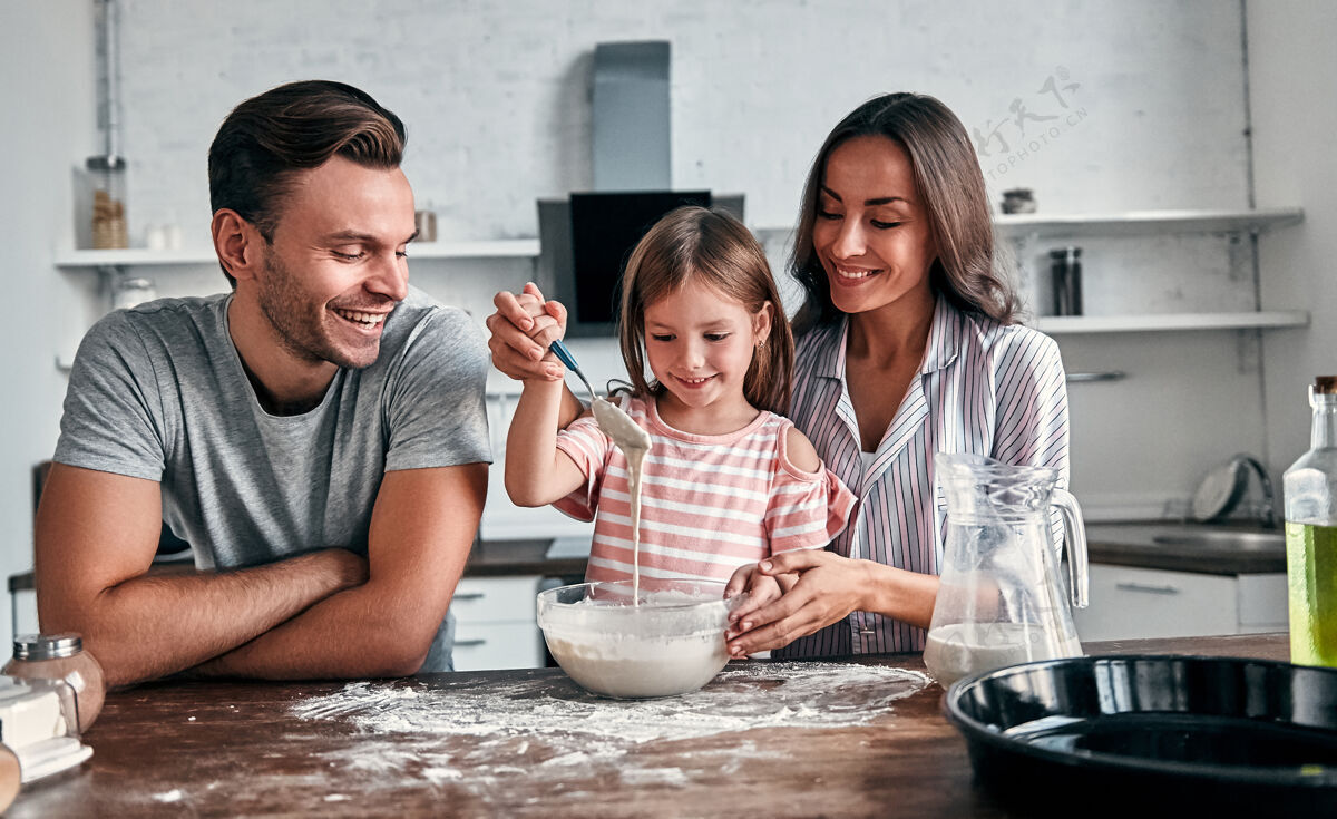 团队合作可爱的小女孩和她美丽的父母在厨房里揉面粉烤面包 一边微笑着做饭女人烘焙卷