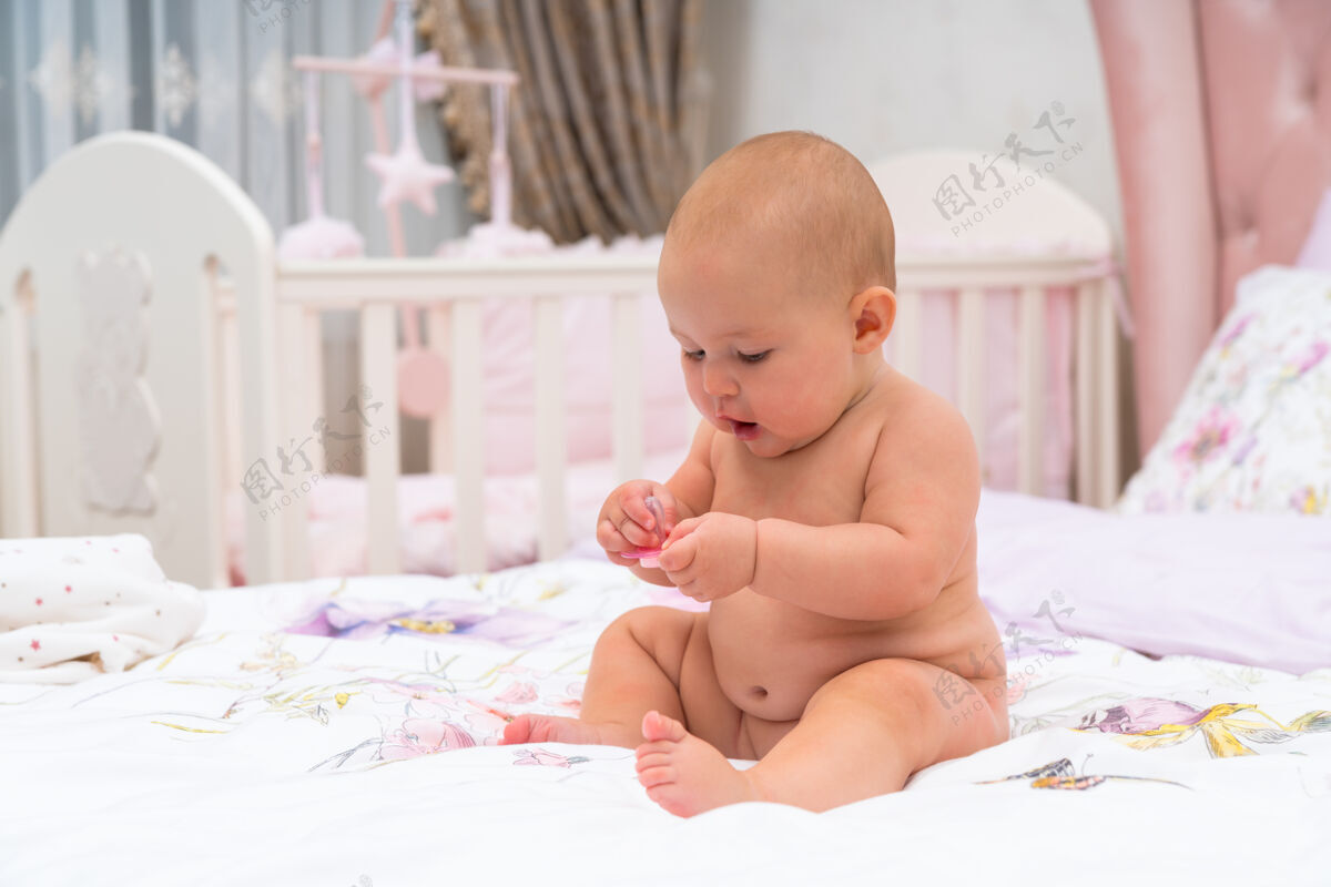 肖像一个快乐的胖乎乎的 没穿衣服的小女婴在托儿所的小床上玩耍 这是一张特写照片玩耍裸露兴趣