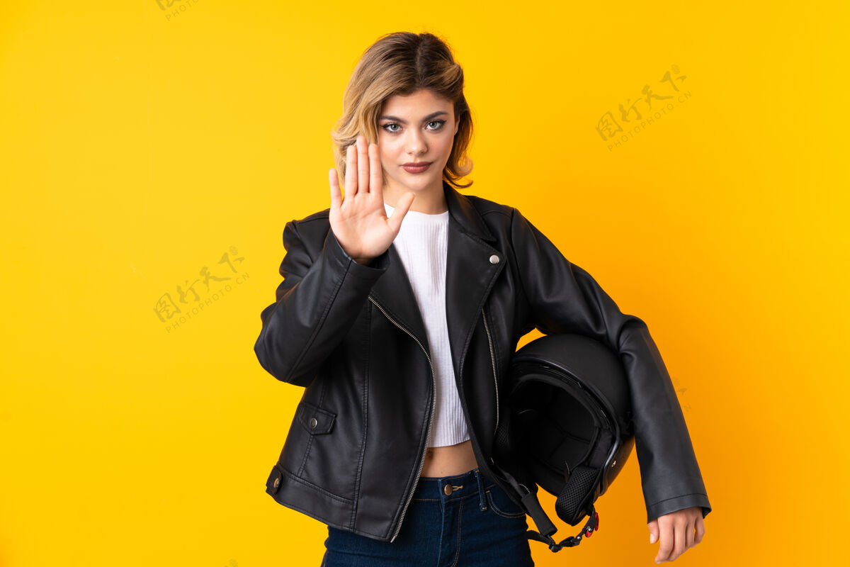 金发一个手持摩托车头盔的少女用手做着停车的手势青少年司机停车