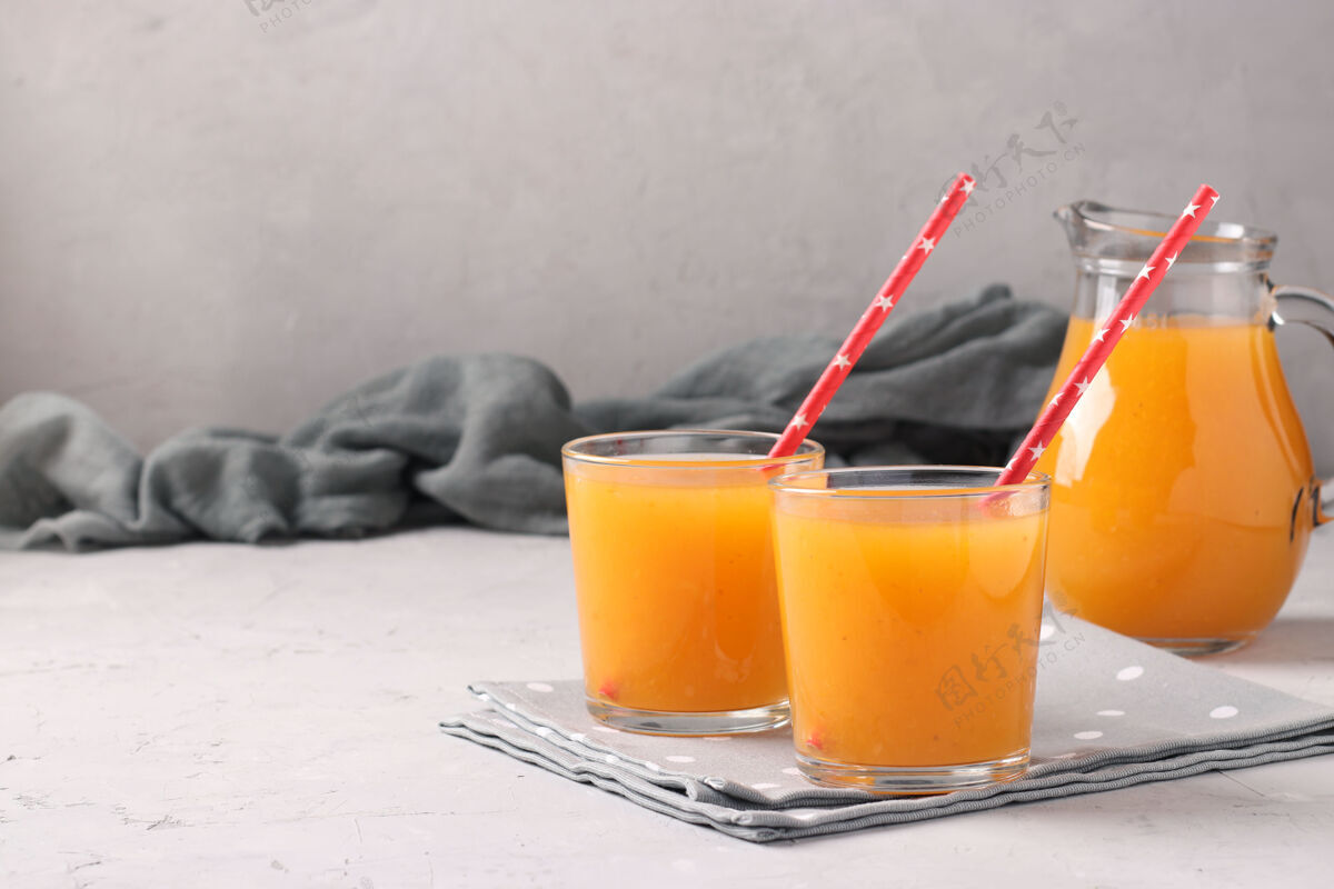 甜杏汁果肉在两个玻璃杯和一个罐子上的灰色表面与地方的文字 水平格式素食果汁香料