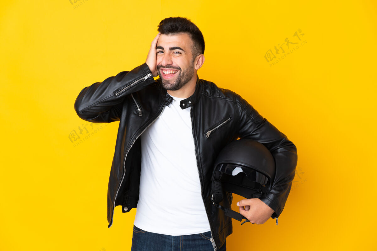 胡须一个戴着摩托车头盔的高加索男人在孤立的黄色背景下笑了很多摩托车大笑男性